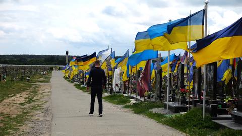 Mourning man go among countless graves of ukrainian soldiers with national flags at military cemeter