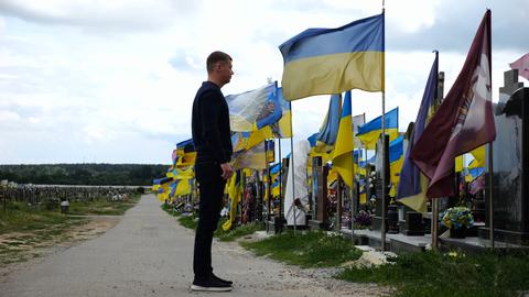 Mourning man standing among countless graves of ukrainian soldiers with national banners pay tribute