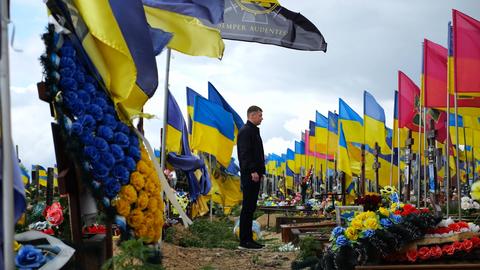 Mourning man standing among countless graves of ukrainian soldiers with national banners pay tribute