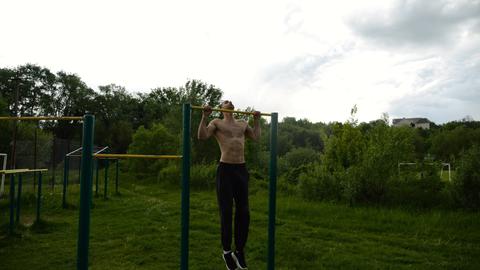 Muscular athlete doing pull ups on horizontal bar at sports ground. Young shirtless sportsman exerci