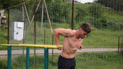 Young sportsman doing push ups on parallel bars at nature. Strong sporty man exercising at sports gr