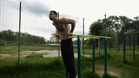 Young sportsman doing push ups on parallel bars at nature. Strong sporty man exercising at sports gr
