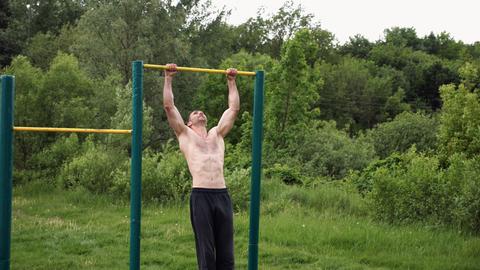 Muscular athlete doing pull ups on horizontal bar at sports ground. Young shirtless sportsman exerci