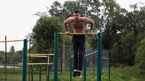 Hardy shirtless sportsman doing push ups on horizontal bar at nature. Strong and muscular guy traini