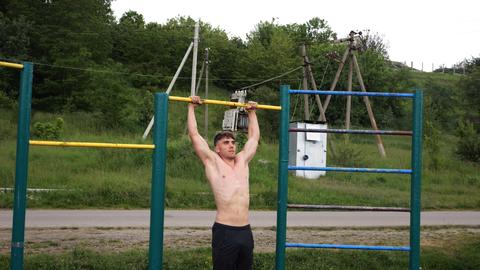 Muscular athlete doing pull ups on horizontal bar at sports ground. Young shirtless sportsman exerci
