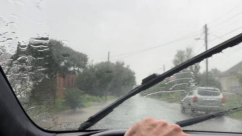 POV of male hand on steering wheel driving a car during a heavy rain on rural road. Detailed view fr