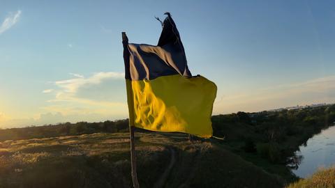 National flag of Ukraine waving on hilltop against a bright golden sunset. View of Ukrainian banner 