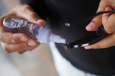 Hands spraying clear cleaning solution onto eyeglass lens for maintenance and sm