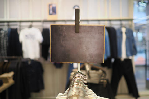 Blank rectangular chalkboard sign above clothing rack in retail store viewing