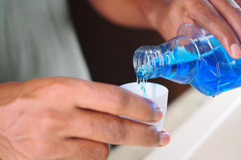 Hands pouring bright blue mouthwash into white cap for oral rinse use