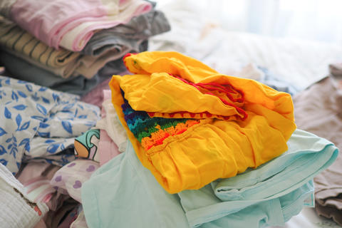 Folded yellow child's dress with rainbow crochet detail on pastel clothing pile