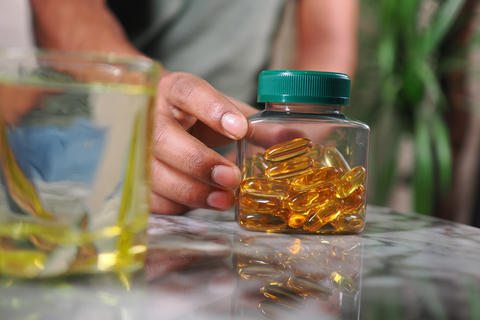 Hand holding jar of fish oil capsules on reflective table