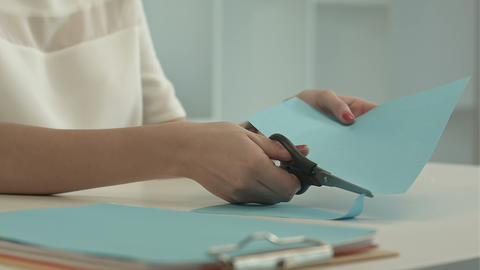 Girl is cutting color blue paper with scissors
